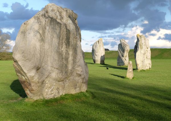 Zeigt einen historischen Steinkreis. Mehrere große Steinblöcke kreisförmig auf einer Wiese angeordnet